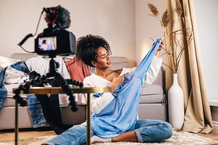 Une femme présente un vêtement bleu devant une caméra, illustrant le rôle d’ambassadrice mode dans un cadre chaleureux