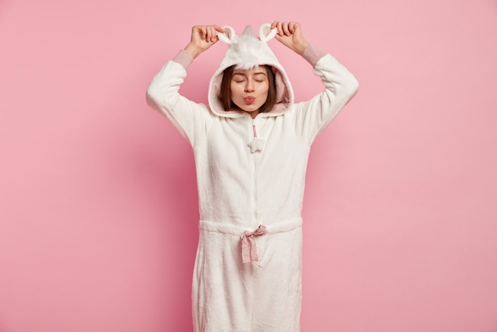 Femme en peignoir blanc à capuche licorne sur fond rose, vêtement ludique parmi les accessoires de sommeil fantaisie
