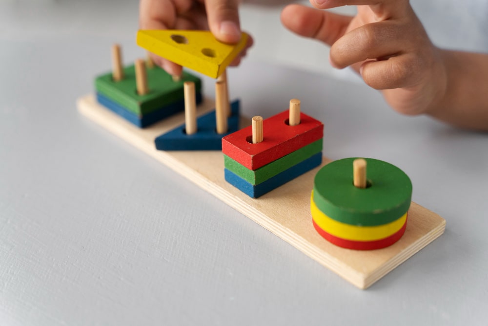 Une main d'enfant tenant délicatement un bloc de "construction Montessori", un jeu en bois qui favorise l'apprentissage sensoriel et la motricité fine