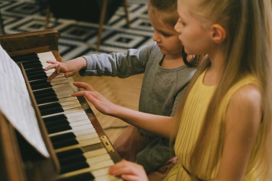 Deux enfants apprennent le piano ensemble en suivant une partition.