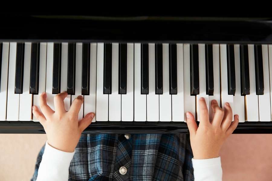 Apprendre le piano dès le plus jeune âge Un enfant apprend le piano en posant ses mains sur les touches noires et blanches.