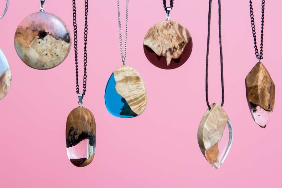 Collection de pendentifs artisanaux en bois et résine époxy suspendus sur fond rose.