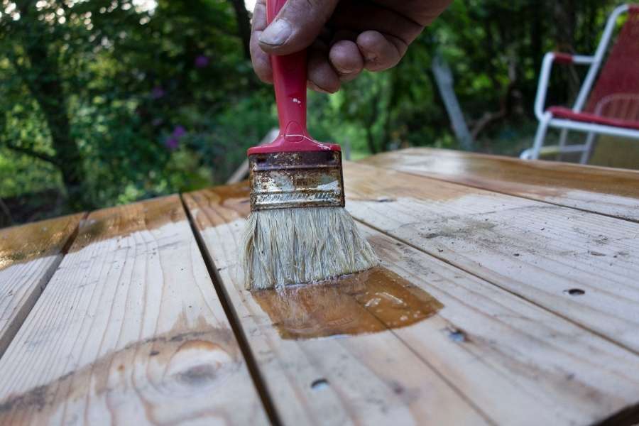 Application de finitions huilées sur une surface en bois clair en extérieur.