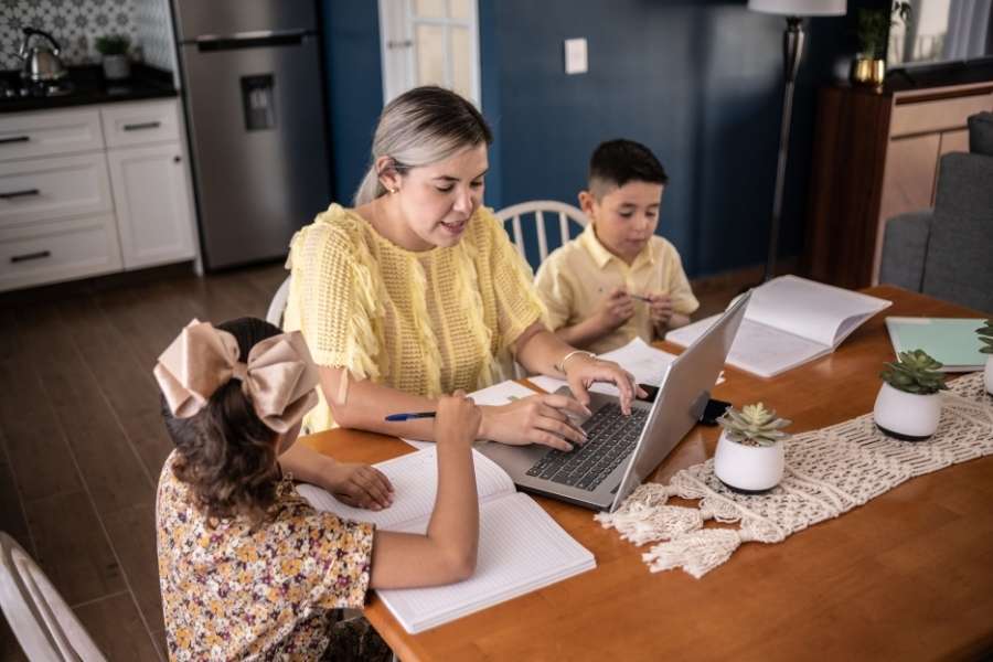 Étudier à distance grâce à la formation en alternance. Femme et enfants travaillant à domicile sur un ordinateur, symbole de la flexibilité de la formation en alternance.