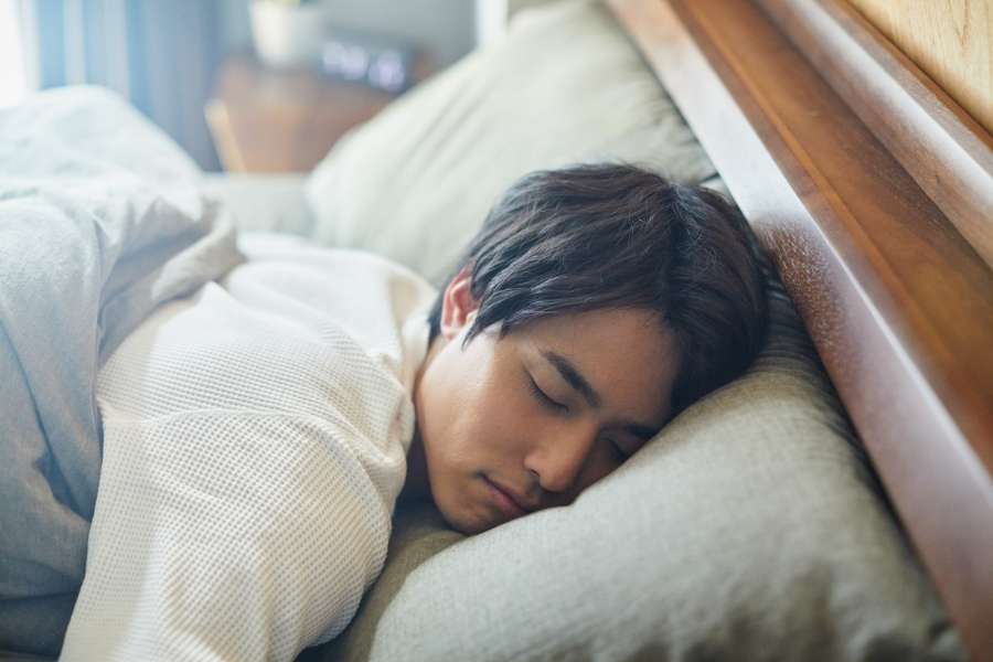 Homme dormant profondément – Interpréter les rêves récurrents Homme endormi paisiblement dans son lit, symbole de repos et de rêves récurrents.