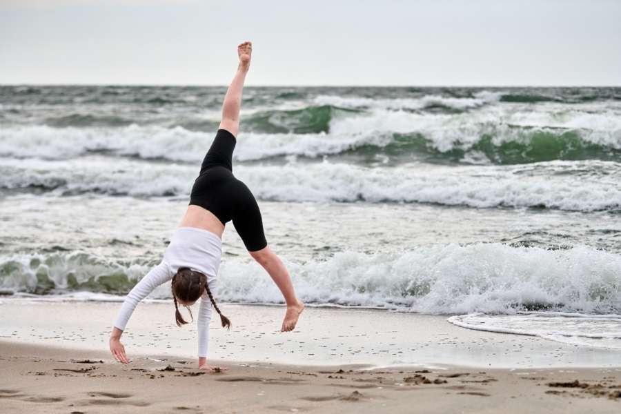Purification énergétique – Nettoyer énergétiquement son espace de vie Jeune femme effectuant un mouvement de yoga sur la plage pour nettoyer énergétiquement son espace intérieur et se ressourcer.