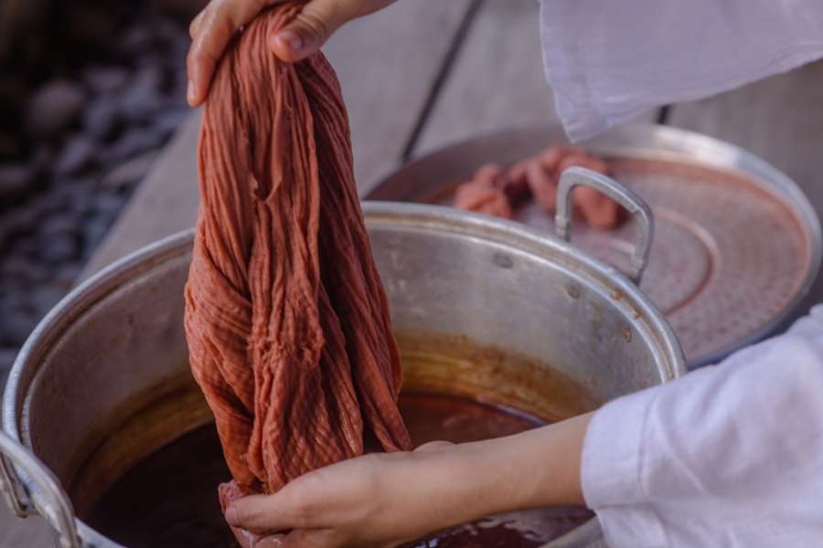 Fabrication artisanale de teinture naturelle des tissus. Une personne trempe un tissu dans une marmite contenant une teinture naturelle des tissus.