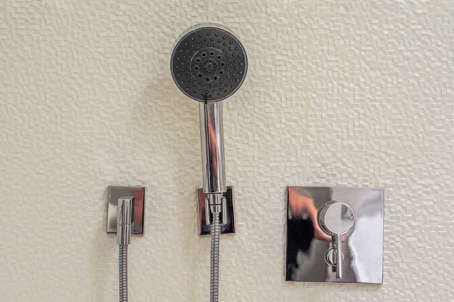 Pomme de douche et commande de mitigeur thermostatique installées sur un mur de salle de bain.