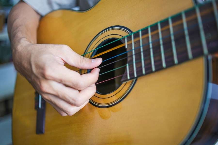 Apprendre à jouer sur sa première guitare acoustique Une main joue les cordes d’une première guitare acoustique en bois naturel.