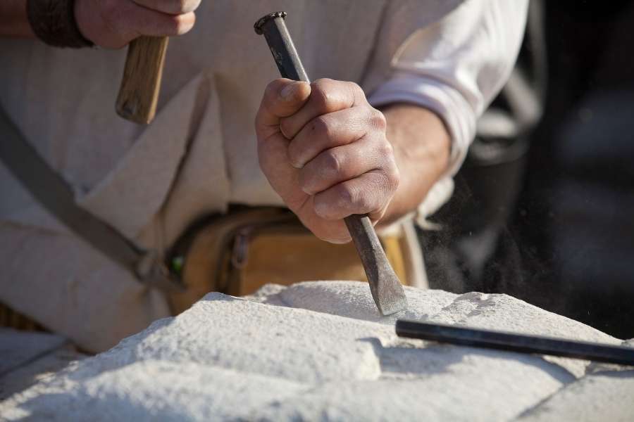 Artisan en pleine sculpture sur pierre. Un artisan sculpteur taille la pierre à l’aide d’un burin et d’un marteau, illustrant la sculpture sur pierre.