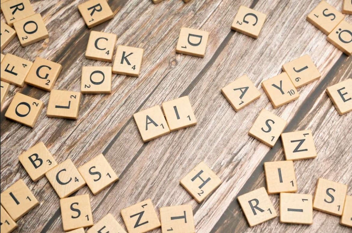 Des lettres en bois de type Scrabble éparpillées sur une table rustique, avec les lettres A et I mises en avant pour illustrer un guide débutant IA.