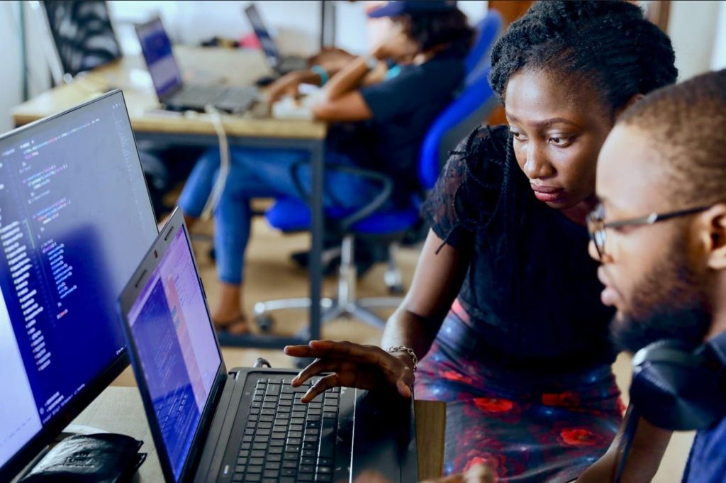 Deux jeunes développeurs, un homme et une femme, collaborent intensément sur du code informatique dans un bureau moderne, illustrant le dynamisme de la tech Afrique IA 2026.