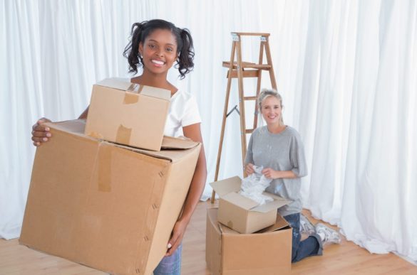 Deux jeunes femmes souriantes emballent des cartons dans un salon lumineux pour préparer leur projet de devis déménagement