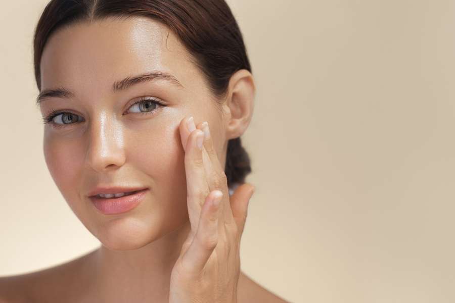 Gros plan d'une femme souriante touchant sa joue, illustrant comment se réveiller avec une peau éclatante grâce à une bonne routine de nuit.