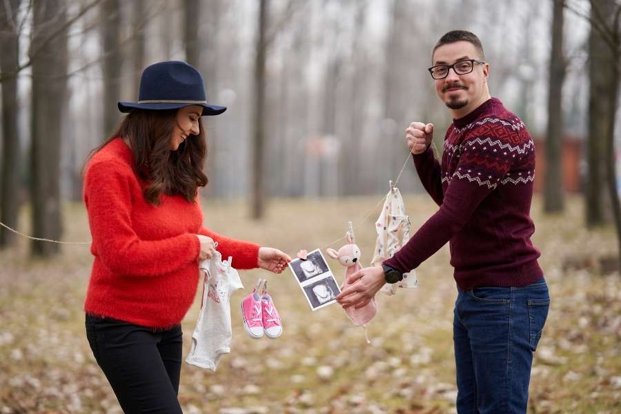 Un couple heureux tient des vêtements de bébé et une échographie pour annoncer sa grossesse en extérieur.