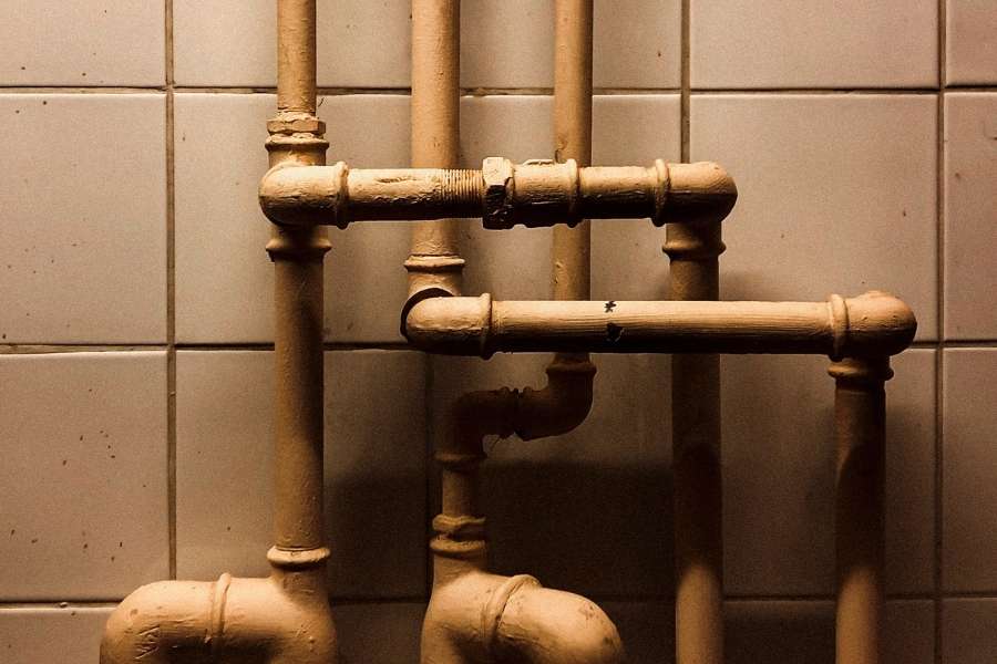 Un réseau complexe de vieilles canalisations métalliques jaunâtres contre un mur carrelé, nécessitant des mesures pour protéger ses canalisations.