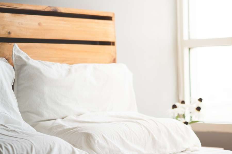 Un lit confortable avec une tête de lit en bois claire baigné par la lumière du soleil.