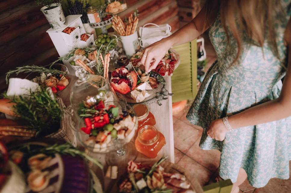 Une mariée en robe verte se sert à un buffet de mariage rustique composé de charcuteries, fromages, herbes fraîches et fruits, une illustration parfaite d'idées mariage écoresponsable et zero dechet.