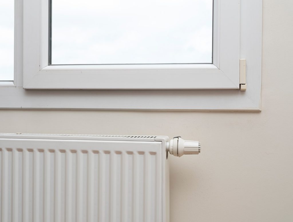 Un radiateur blanc équipé d'un robinet thermostatique installé sous une fenêtre, illustrant le principe chaudière condensation chauffage.